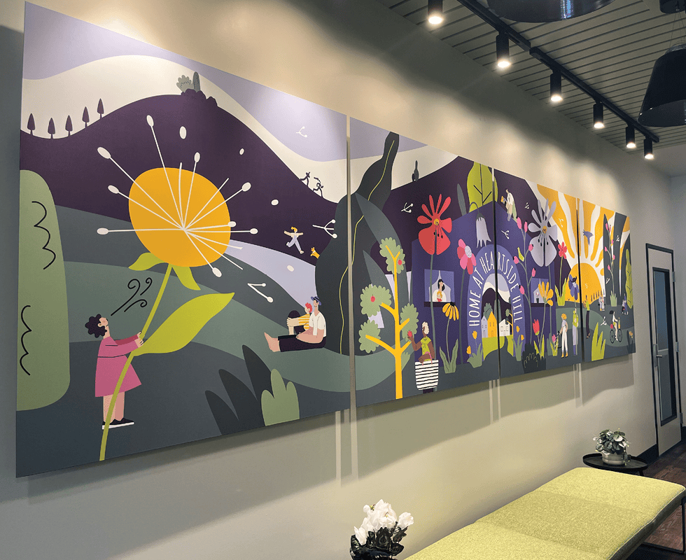 A colorful mural features whimsical, stylized people and large flowers in a vibrant outdoor landscape, with hills, plants, and playful scenes, mounted on a modern wall beneath spotlights.